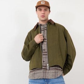 Model with Carhartt Backley Logo Cap in Hamilton Brown, five-panel style with flat peak, styled with olive jacket and plaid shirt