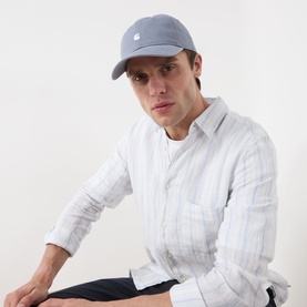 Model with Carhartt Madison Logo Cap in Shady Blue, curved visor, embroidered logo, paired with striped linen shirt