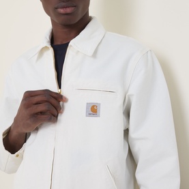 Model wearing Carhartt Detroit Casual Jacket in Wax, showing front zip, chest pocket, and orange logo badge on heavyweight canvas fabric.