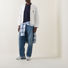 Model wearing Carhartt Detroit Casual Jacket in Wax white with tonal corduroy collar, styled with navy tee, plaid shirt and blue jeans.