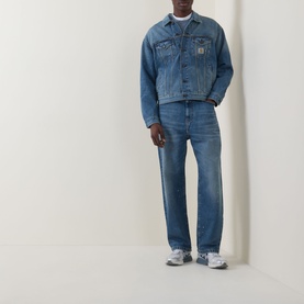 Model wearing Carhartt Helston Denim Jacket in Blue Splatter mid-wash denim with button front, styled with matching blue denim jeans and grey