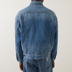 Model wearing Carhartt Helston Denim Jacket in Blue Splatter, rear view, mid-wash heavyweight denim with adjustable hem, styled with matching denim