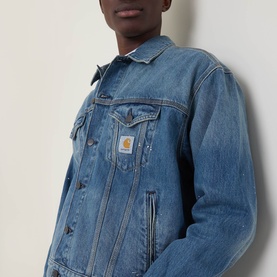 Model wearing Carhartt Helston Denim Jacket in Blue Splatter mid-wash denim with button fastening, flap chest pockets and logo badge.
