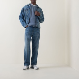 Model wearing Carhartt Helston Denim Jacket in Blue Splatter mid-wash denim with button front, styled with matching jeans and grey trainers.