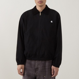Model wearing Carhartt Madison Ripstop Padded Jacket in Black/Wax with corduroy collar, zip fastening, and embroidered logo, styled with grey trousers
