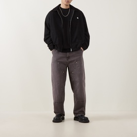 Model wearing Carhartt Madison Ripstop Padded Jacket in Black/Wax with grey wide-leg trousers and black shoes.