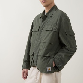 Model wearing Carhartt Mandelson Logo Field Jacket in Leaf green, styled with cream trousers. Multiple flap pockets, tab cuffs, woven logo badge.