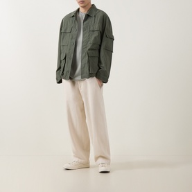 Model wearing Carhartt Mandelson Logo Field Jacket in Leaf green with cream wide-leg trousers and white low-top trainers.