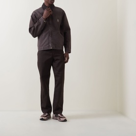 Model wearing Carhartt OG Detroit Logo Jacket in Tobacco, with matching dark trousers and chunky trainers. Zip-front, shirt collar, logo badge.