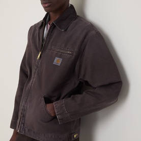 Model wearing Carhartt OG Detroit Logo Jacket in Tobacco, showing chest pocket, front zip, shirt collar and logo badge detail.