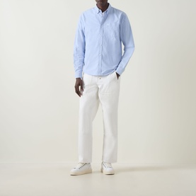 Model wearing Carhartt C-Logo Logo Patch Pocket Shirt in Bleach/White, light blue Oxford fabric, button-down collar, styled with white trousers and