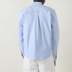Model wearing Carhartt C-Logo Logo Patch Pocket Shirt in Bleach/White, rear view showing box pleat, buttoned cuffs, styled with white trousers.