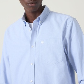 Model wearing Carhartt C-Logo Logo Patch Pocket Shirt in Bleach/White, showing button-down collar, chest pocket and embroidered logo detail.