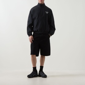 Model wearing Carhartt Travon Logo Windbreaker in black with matching black shorts, black socks and dark chunky trainers.