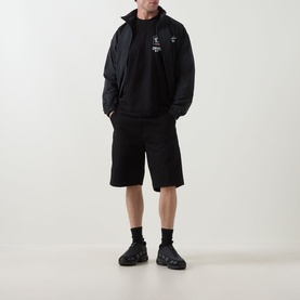 Model wearing Carhartt Travon Logo Windbreaker in black over hoodie, styled with black shorts and chunky trainers