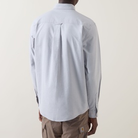 Model wearing Carhartt C-Logo Patch Pocket Shirt in Shady Grey/White, rear view, showing back pleat detail, styled with beige trousers.
