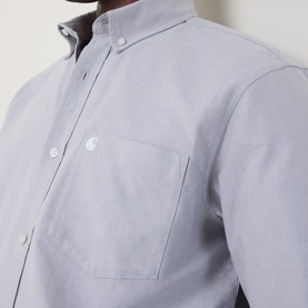 Model wearing Carhartt C-Logo Patch Pocket Shirt in Shady Grey, showing button-down collar, chest patch pocket with embroidered logo detail.