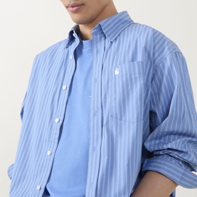 Model wearing Carhartt Keene Stripe Shirt in Curacao blue stripe, showing button fastening, chest pocket and embroidered logo detail.