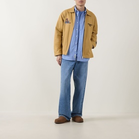 Model wearing Carhartt Keene Stripe Shirt in Curacao blue stripe, styled with tan chore jacket and light wash wide-leg jeans.