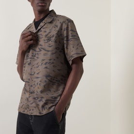 Model wearing Carhartt Travon Duck Feather Print shirt in Cypress/Black, featuring bowling collar, short sleeves, and all-over duck feather print.