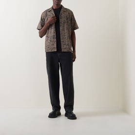 Model wearing Carhartt Travon Duck Feather Print shirt in Cypress/Black with black trousers and black leather shoes.