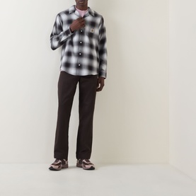 Model wearing Carhartt Tyers Logo Check Print Shirt in black check, with dark brown trousers and chunky trainers.