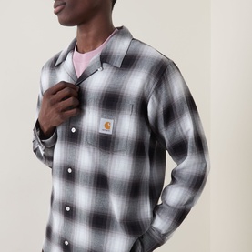 Model wearing Carhartt Tyers Logo Check Print Shirt in black check, with bowling collar and logo badge, styled over a pink T-shirt.
