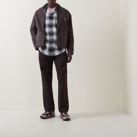 Model wearing Carhartt Tyers Logo Check Print Shirt in Check/Black with matching dark trousers and chunky trainers.