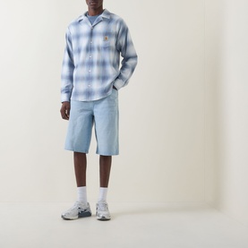 Model wearing Carhartt Tyers Logo Check Shirt in Shady Blue check, styled with light blue denim shorts and grey trainers.