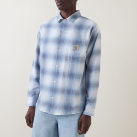 Model wearing Carhartt Tyers Logo Check Print Shirt in Shady Blue check, styled with light blue jeans. Long sleeves, chest patch pocket with logo