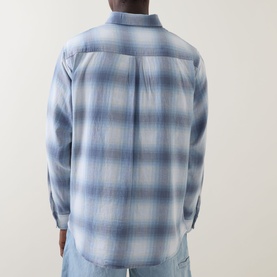 Model wearing Carhartt Tyers Logo Check Print Shirt in Shady Blue check, rear view showing back pleat and long sleeves, styled with light blue jeans