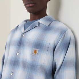 Model wearing Carhartt Tyers Logo Check Print Shirt in Shady Blue check, featuring bowling collar, chest patch pocket with logo badge.
