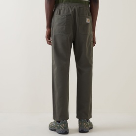 Model wearing Carhartt Flint Casual Trousers in Leaf, showing rear patch pockets and logo badge, styled with grey and yellow trainers