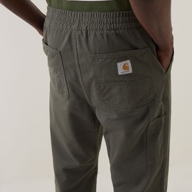 Model wearing Carhartt Flint Casual Trousers in Leaf green, showing rear patch pocket with logo badge and elasticated waistband detail.