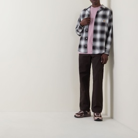 Model wearing Carhartt Master Casual Trousers in Tobacco, mid-rise tapered leg, styled with black check overshirt and pink crew-neck tee.
