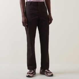 Model wearing Carhartt Master Casual Trousers in Tobacco, tapered-leg cotton cut, styled with chunky trainers and a pink shirt.