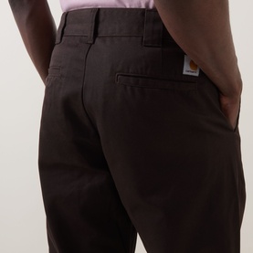 Model wearing Carhartt Master Casual Trousers in Tobacco, rear view showing jetted back pocket with button and logo badge patch.