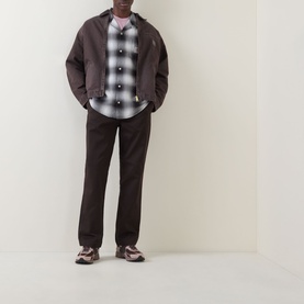 Model wearing Carhartt Master Casual Trousers in Tobacco, styled with a dark zip jacket, check shirt, and chunky trainers.