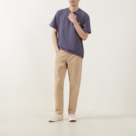 Model wearing Carhartt American Script Logo T-Shirt in Shady Purple, crew neck, short sleeves, styled with beige chinos and white trainers.