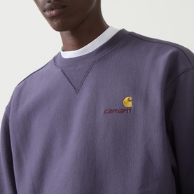 Model wearing Carhartt American Script Logo Sweatshirt in Shady Purple, crew neck with embroidered chest logo, styled with white T-shirt underneath.