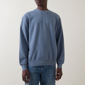 Model wearing Carhartt Caspian Sweatshirt in Shady Blue Heather, crew neck, dropped shoulders, ribbed trims, styled with blue jeans.