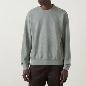 Model wearing Carhartt Caspian Sweatshirt in Shady Green Heather, crew neck, dropped shoulders, ribbed trims, styled with dark trousers.