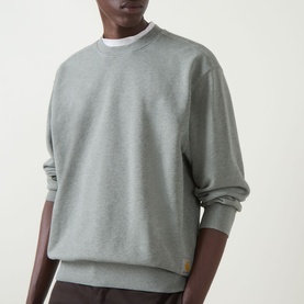 Model wearing Carhartt Caspian Sweatshirt in Shady Green Heather, crew neck, dropped shoulders, ribbed trims, styled with dark trousers.