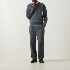 Model wearing Carhartt Chase Logo Sweatshirt in Styx/Gold with matching grey trousers and black loafers.