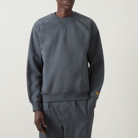 Model wearing Carhartt Chase Logo Sweatshirt in Styx/Gold, crew neck, heavyweight cotton blend with embroidered logo above cuff, styled with striped