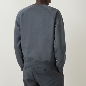 Model wearing Carhartt Chase Logo Sweatshirt in Styx/Gold, slate blue crew neck sweatshirt, back view, styled with pinstripe trousers