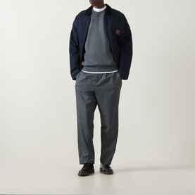 Model wearing Carhartt Chase Logo Sweatshirt in Styx/Gold grey, styled with navy bomber jacket and grey tapered trousers.