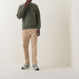 Model wearing Carhartt Chase Logo Sweatshirt in Leaf/Gold with beige chinos and grey trainers.