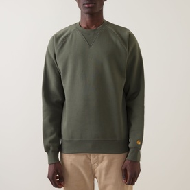 Model wearing Carhartt Chase Logo Sweatshirt in Leaf/Gold, crew neck with V-shaped insert, gold embroidered logo above cuff, styled with beige