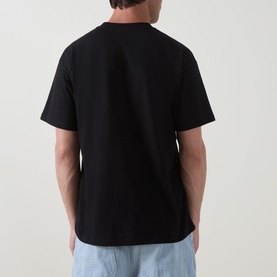 Model wearing Carhartt Cheese Toast T-Shirt in Black, rear view, crew neck, short sleeves, straight hem, paired with light blue jeans.